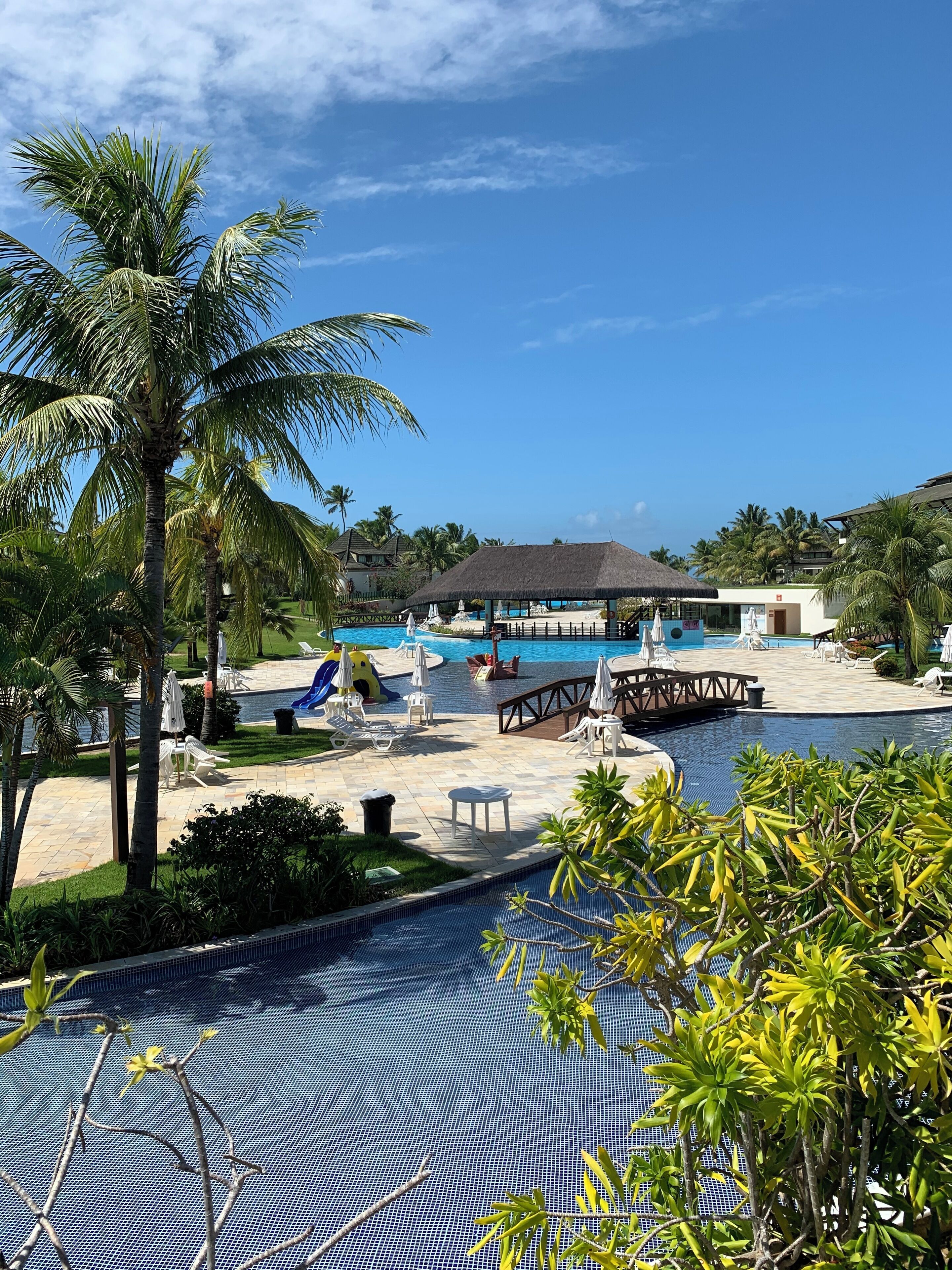 A resort pool area with lounge chairs, a thatched-roof structure, and a view of the beach and ocean.