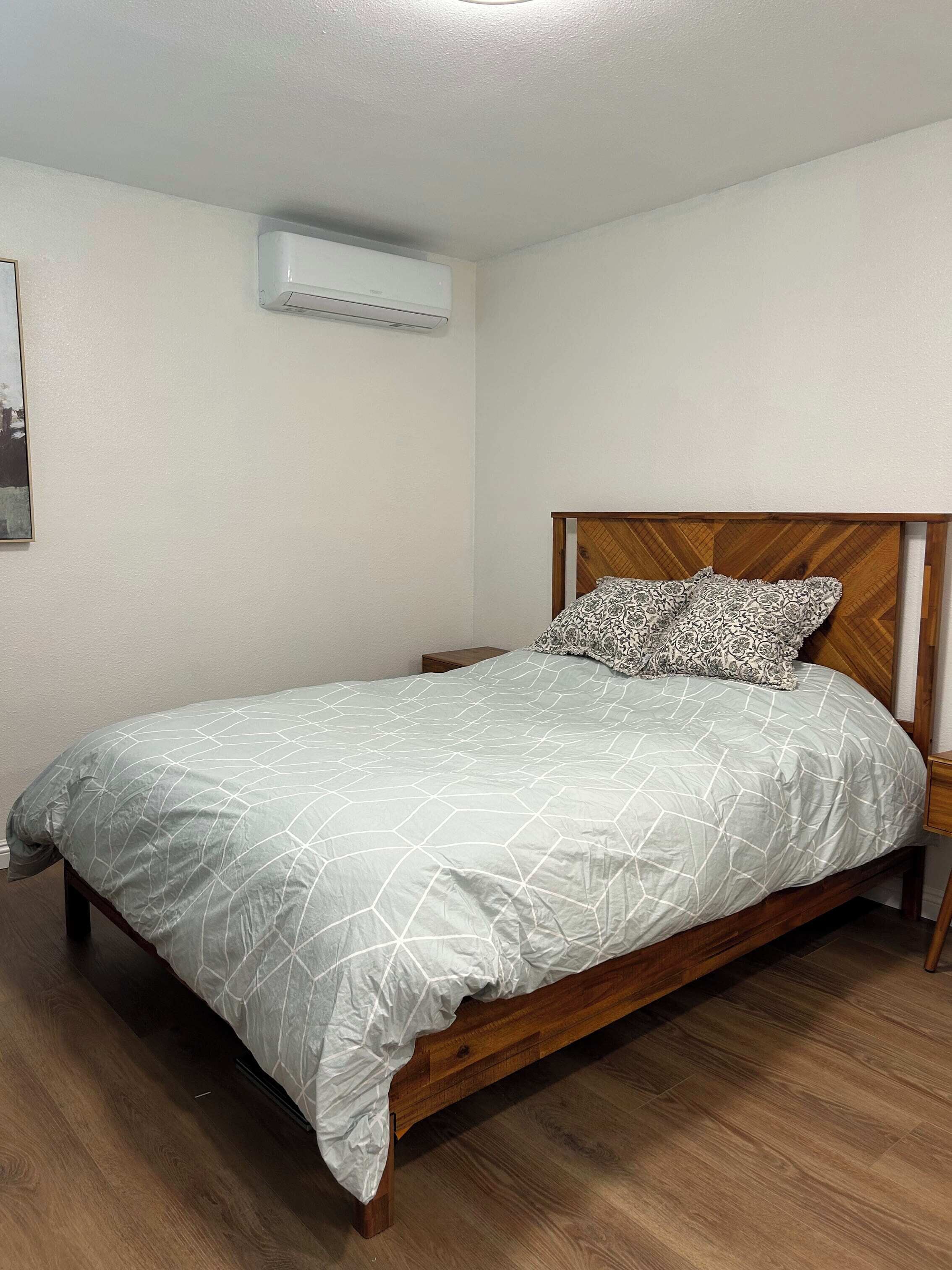 Un letto singolo con copriletto a motivi geometrici, una testiera in legno e un cuscino abbinato. Un condizionatore d'aria è fissato alla parete sopra il letto.