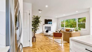 Uma cozinha moderna com uma geladeira grande, uma sala de jantar com mesa de madeira e uma sala de estar com sofá e televisão.