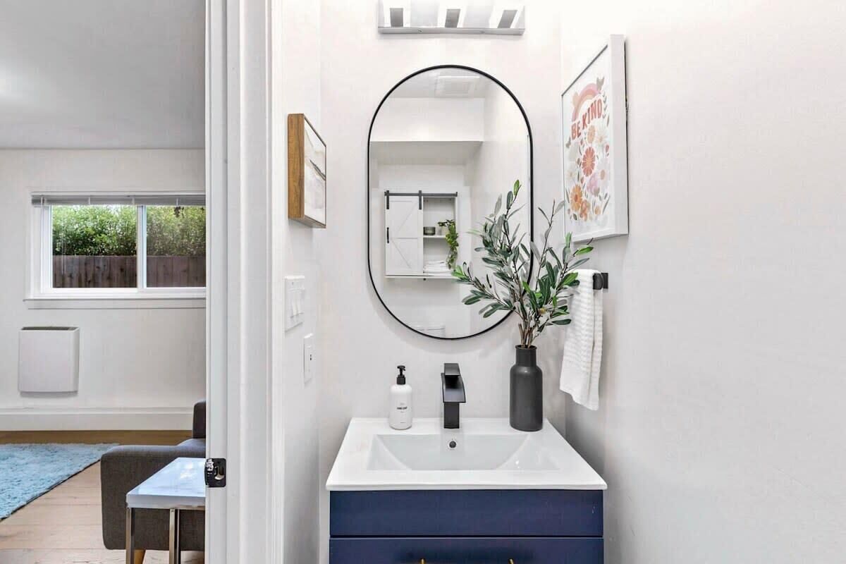 Un bagno moderno con un lavandino bianco, un mobile portaoggetti blu scuro e uno specchio rotondo.