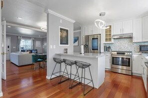 A modern kitchen with white cabinets, stainless steel appliances, and a bar area with stools. - Marbella Lane - Buckingham Place Laundry P (Pacifica)