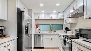 A modern kitchen with white cabinets, stainless steel appliances, and gold handles. - Marbella Lane-Cozy Luxury Townhome near Microsoft (Bellevue)