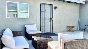 Une terrasse dotée de meubles en osier, d’une table en verre et d’un portail en métal.