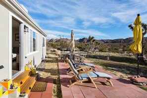 A patio with lounge chairs and a table, a covered area with a yellow umbrella, and a view of mountains in the background. - Marbella Lane - 10 Acres Oasis Desert Retreat! (Joshua Tree)