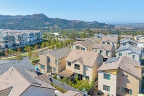 Un quartier résidentiel avec des maisons modernes, un ciel dégagé et des collines qui se dessinent à l’horizon.