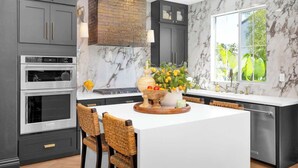 A modern kitchen with dark cabinets, a marble backsplash, and a large window with a view of greenery. - Marbella Lane - Stylish Dream Home in RMV w Pool (Mission Viejo)