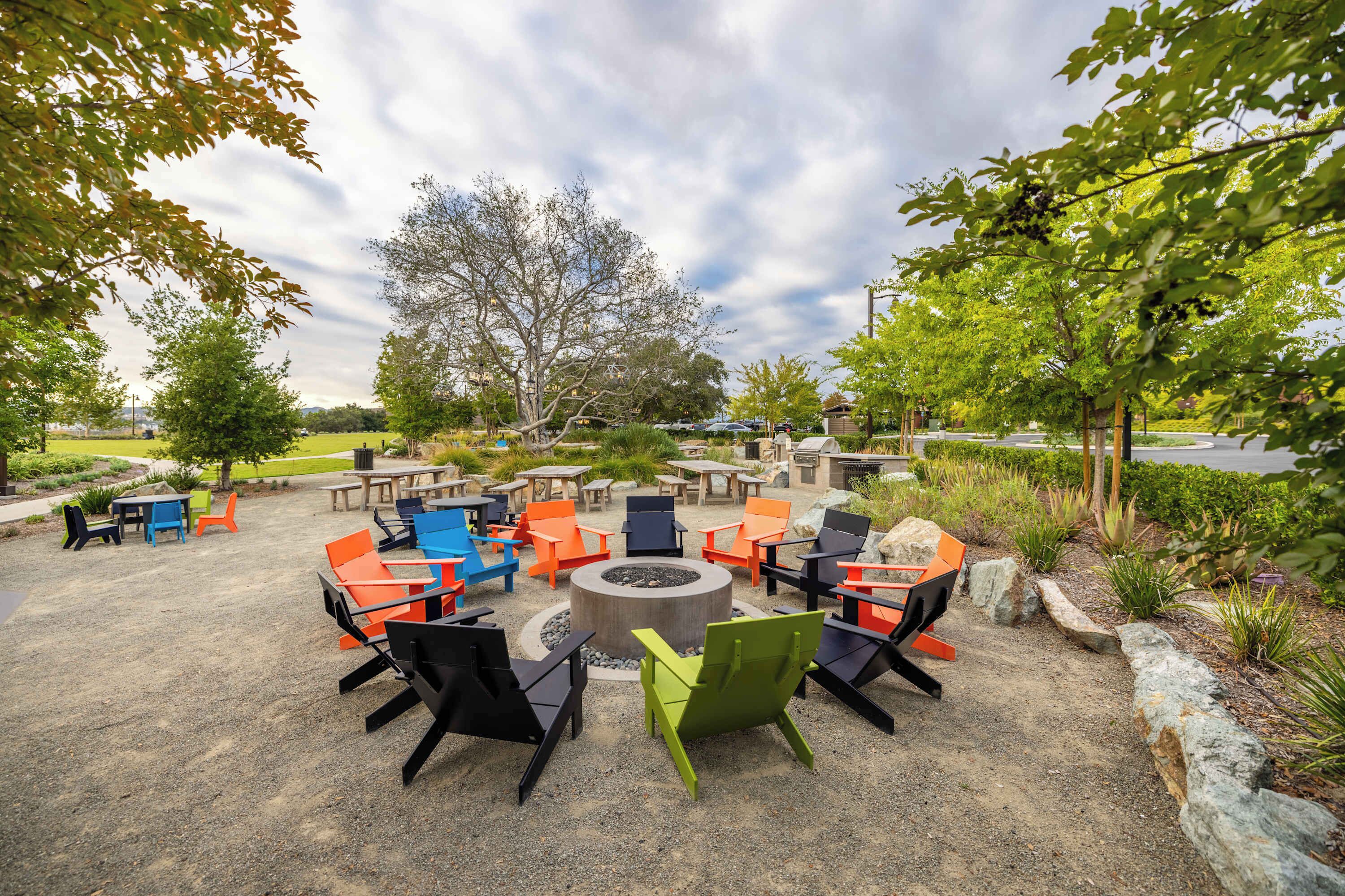 An outdoor seating area with colorful chairs and tables arranged around a central fire pit.