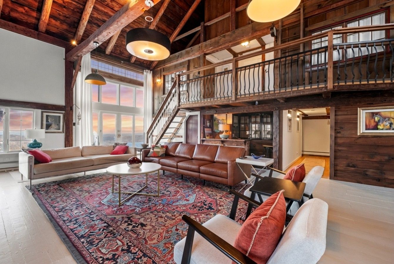 A spacious living area with a large rug, leather sofas, a coffee table, and a staircase leading to an upper level.