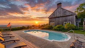 En swimmingpool med liggestole, et træhus og udsigt til solnedgang.