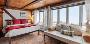 A bedroom with a bed, a sofa, a window with curtains, and a wooden ceiling.