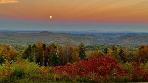 Un paysage montagneux, avec un coucher de soleil et une maison visible au loin.
