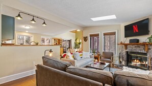 A cozy living room with a fireplace, a flat-screen TV mounted above it, and a comfortable seating area with sofas and a coffee table. - Bear Den: Hot Tub + Secluded | Sleeps 8 | Modern (Wardsboro)