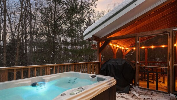 A hot tub on a wooden deck with a covered outdoor seating area and string lights. - Bear Den: Hot Tub + Secluded | Sleeps 8 | Modern (Wardsboro)