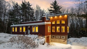 A two-story cabin with a snow-covered roof, surrounded by a forest. - Bear Den: Hot Tub + Secluded | Sleeps 8 | Modern (Wardsboro)