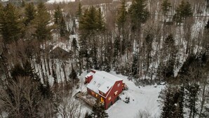 Eine rote Holzhütte, umgeben von dichtem Wald mit verschneitem Boden.