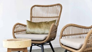 Twee rieten stoelen met kussens en een klein houten krukje.