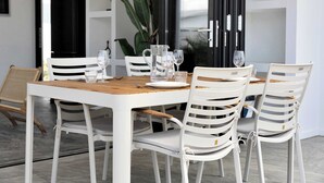 Een eethoek met een witte tafel en stoelen, een zwarte koelkast en een grote plant op de achtergrond.