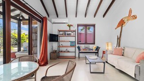 A modern living room with a glass table, wicker chairs, a sofa, and a bookshelf. - Boat House with air conditioning in the living room and communal pool (Kralendijk)