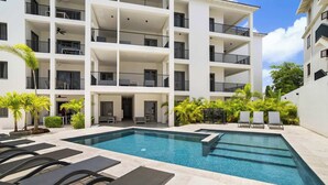 A modern multi-story building with a swimming pool, outdoor seating, and lush greenery. - Bonaire Beach Apartments 14 with spectacular sea views and beautiful sunsets every evening (Kralendijk)