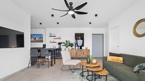 A modern living room with a sofa, a dining area with chairs, a coffee table, a ceiling fan, and a large window. - Bonaire Beach Apartments 14 with spectacular sea views and beautiful sunsets every evening (Kralendijk)