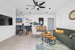 Ein modernes Wohnzimmer mit einer Couch, einem Essbereich mit Stühlen, einem Couchtisch, einem Deckenventilator und einem großen Fenster.