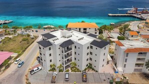 A multi-story building with a flat roof, adjacent to a waterfront with clear blue water and a pier. - Bonaire Beach Apartments 14 with spectacular sea views and beautiful sunsets every evening (Kralendijk)