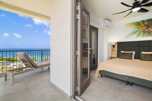 A balcony with a view of the ocean, a bed with a green headboard, and a ceiling fan. - Bonaire Beach Apartments 14 with spectacular sea views and beautiful sunsets every evening (Kralendijk)