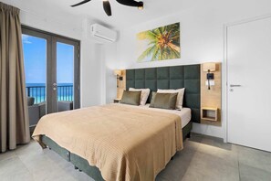 Ein modernes Hotelzimmer mit einem großen Bett, einem Balkon mit Blick, einem Deckenventilator und Wandbildern im tropischen Stil.