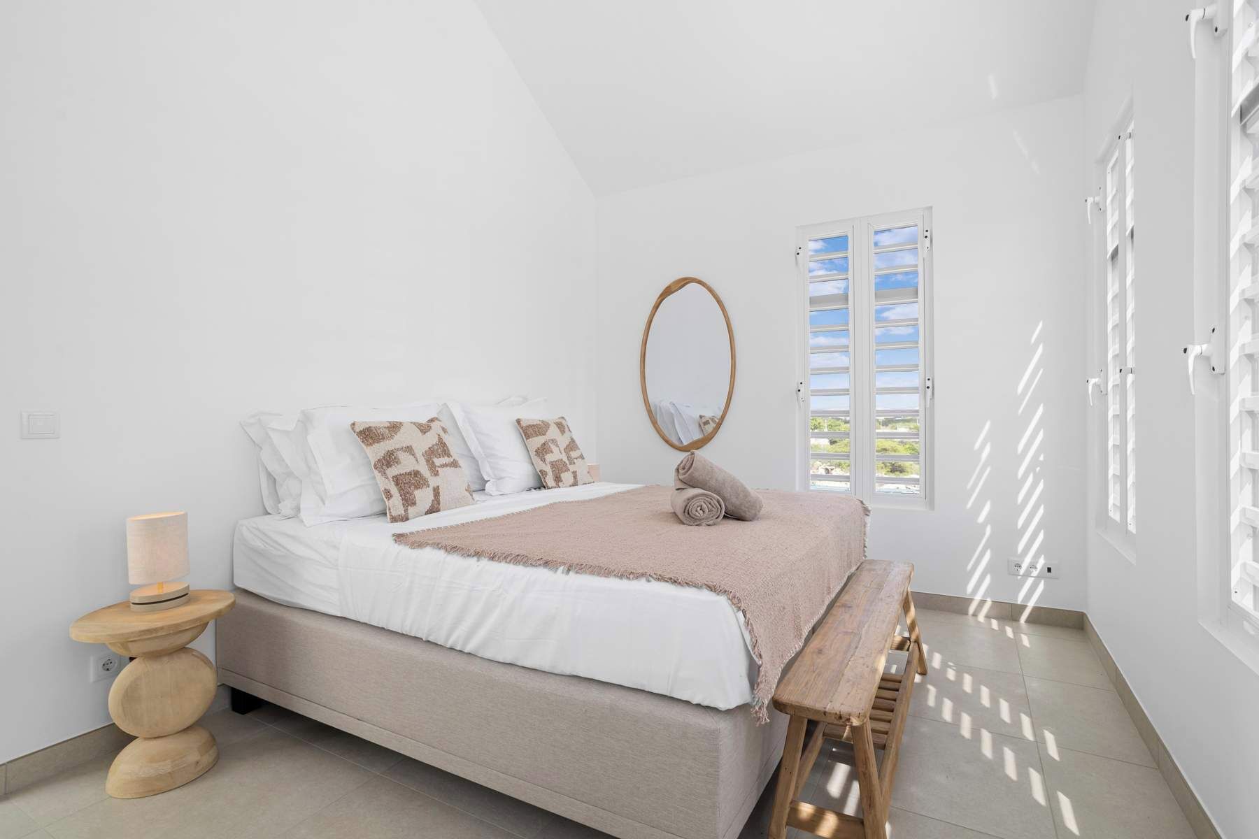 Un dormitorio con cama, mesita de noche, espejo y ventana con persianas.