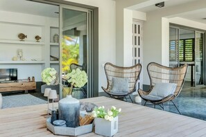 Un salon moderne avec une table en bois, deux fauteuils en osier, un téléviseur et des objets décoratifs.