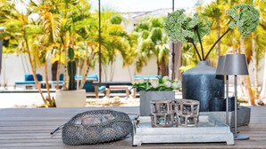 Una terraza de madera con una cesta de metal, un candelabro de vidrio y un florero con follaje verde.