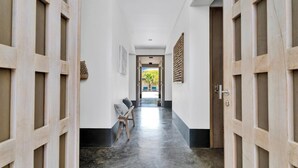 Un pasillo con puertas de madera, un banco y vistas a un espacio exterior con sillas.