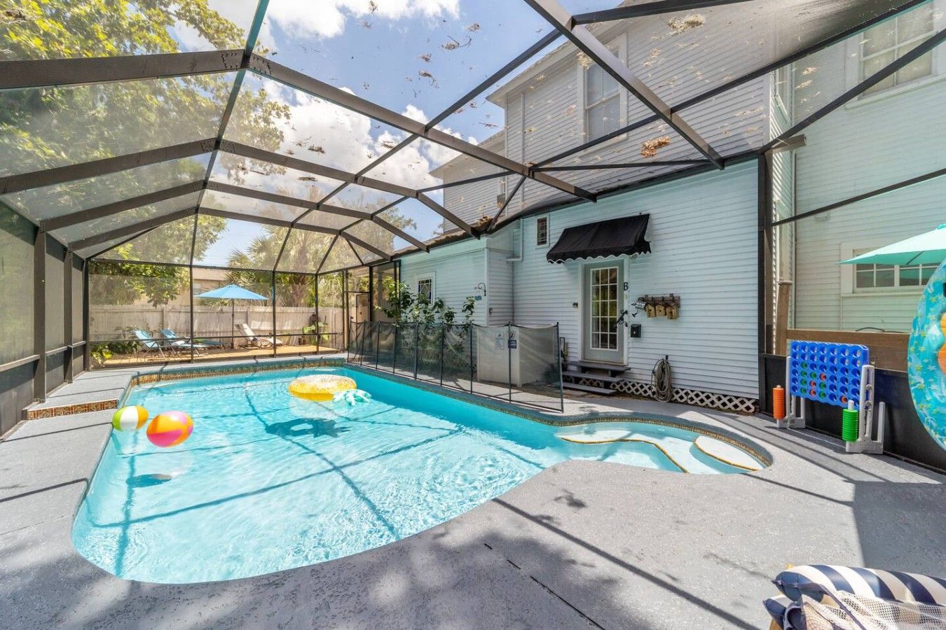 Une piscine intérieure abritée par une structure en verre, entourée d’une maison à l’extérieur blanche et dotée d’un auvent noir au-dessus de la porte.