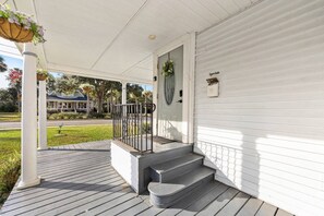 A porch with a white railing, a set of steps leading to a door, and a hanging flower basket.
