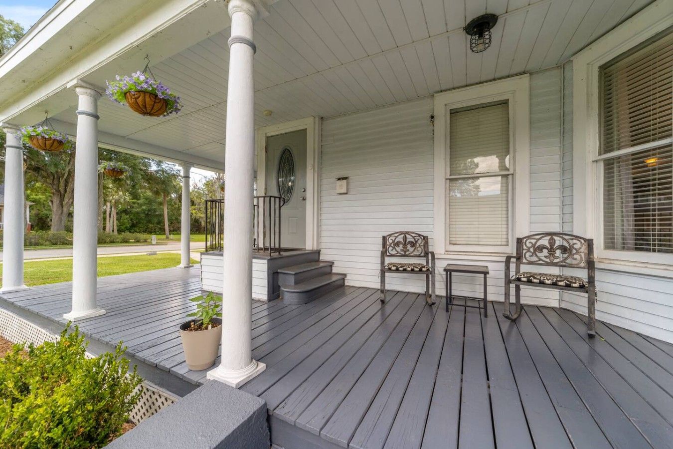 A porch with white columns, a bench, a small table, and hanging flower baskets.