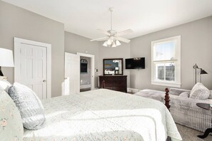 A bedroom with a large bed, a dresser, a television, and a ceiling fan. - Martin House | Historic Poolside Upper Suite 2/1 (Ocala)
