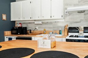 A kitchen with white cabinets, a wooden countertop, a stove, and a welcome card on the table. - Martin House | Historic Poolside Upper Suite 2/1 (Ocala)