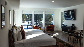 A modern hotel room with a large bed, two chairs, a desk, and a TV.