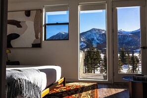 Ein Schlafzimmer mit Bett, großem Fenster, Blick auf schneebedeckte Berge und einem Balkon mit Geländer.