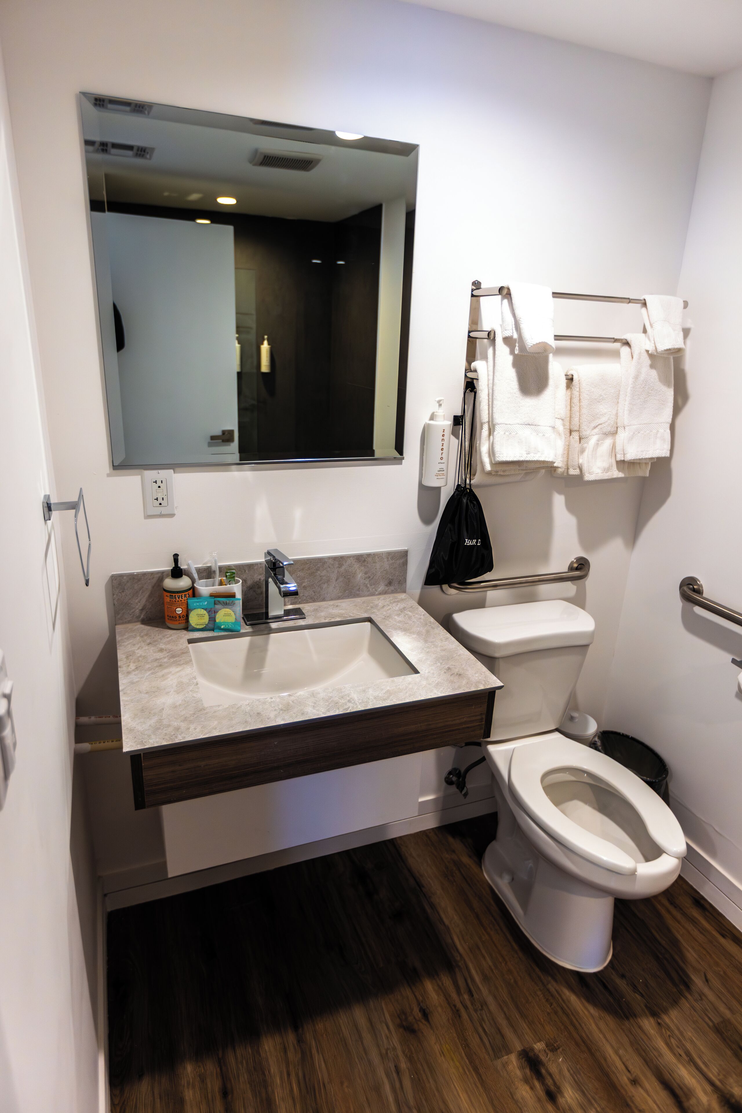 A modern bathroom with a sink, mirror, toilet, and handrails.