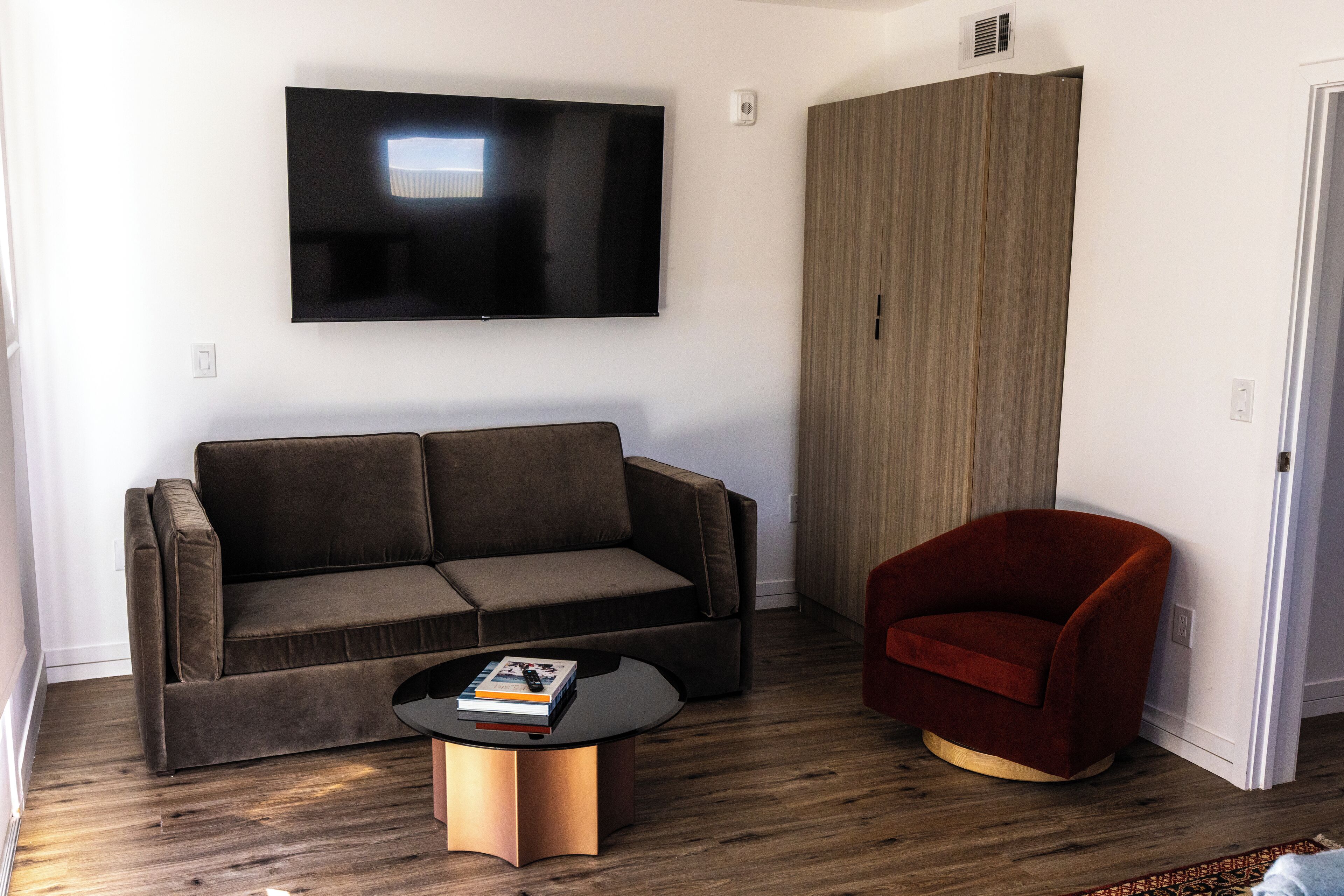 A modern living room with a sofa, a red armchair, a coffee table with books, and a flat-screen TV mounted on the wall.