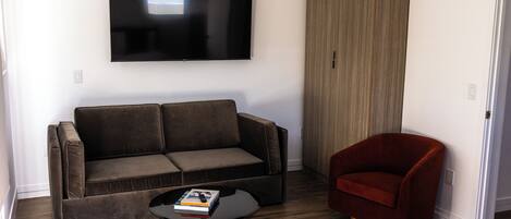 A modern living room with a sofa, a red armchair, a coffee table with books, and a flat-screen TV mounted on the wall.