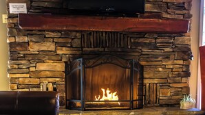 A stone fireplace with a TV above it, leather chairs in front, and a sign advising against wood use.