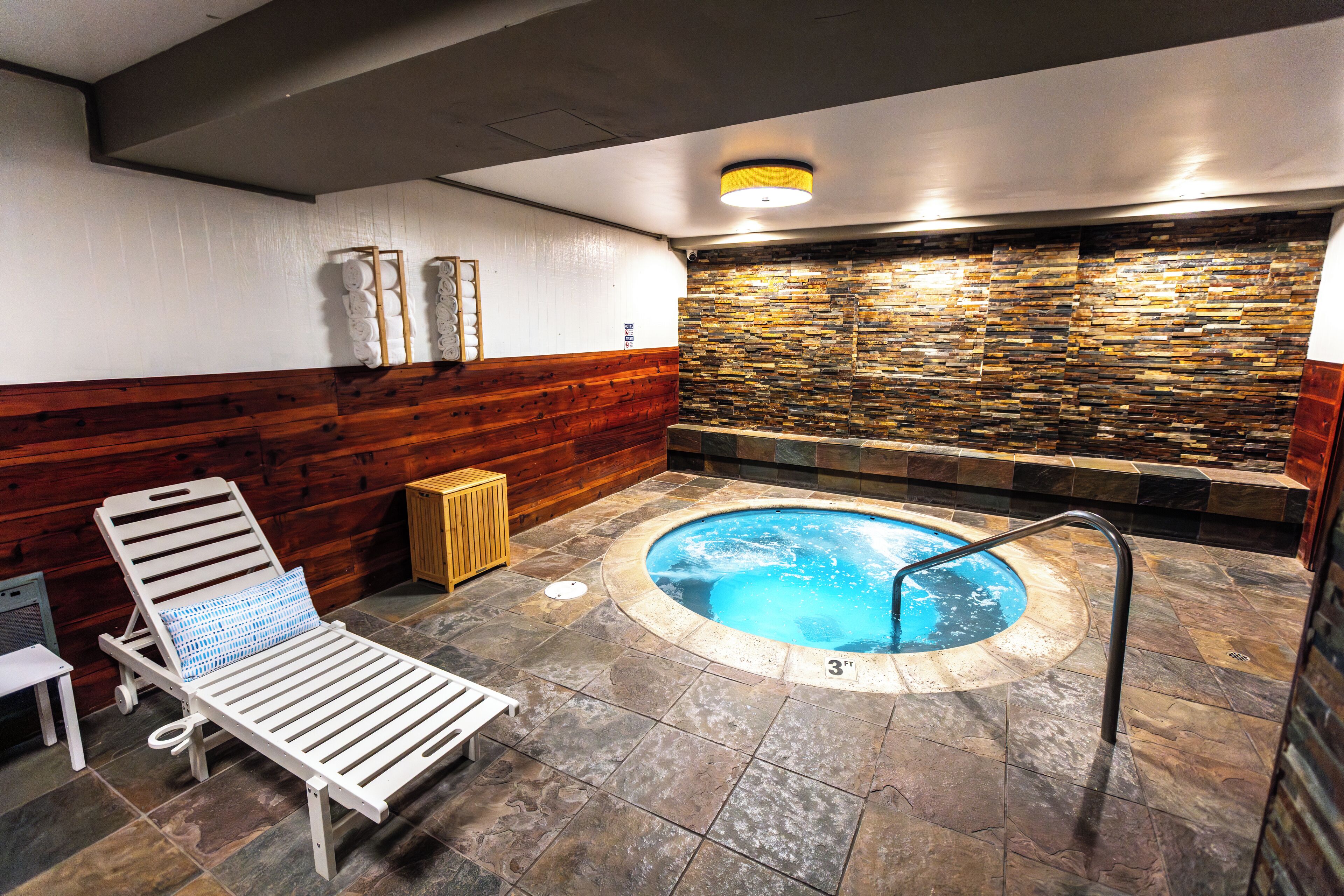Un'area benessere con vasca idromassaggio, rivestimenti in legno a pannelli e una poltrona relax.