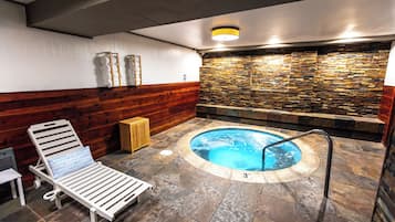 Un'area benessere con vasca idromassaggio, rivestimenti in legno a pannelli e una poltrona relax.