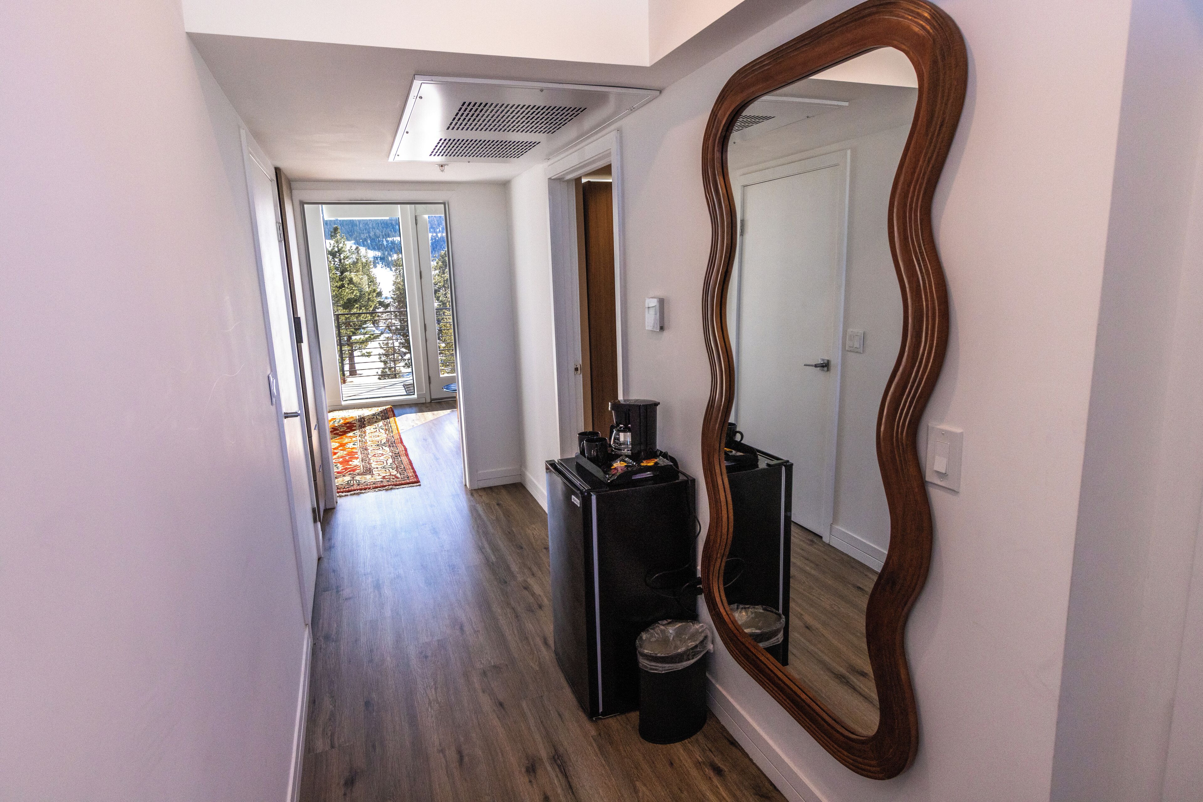 A hallway with a wooden floor, a large mirror, and a compact refrigerator.
