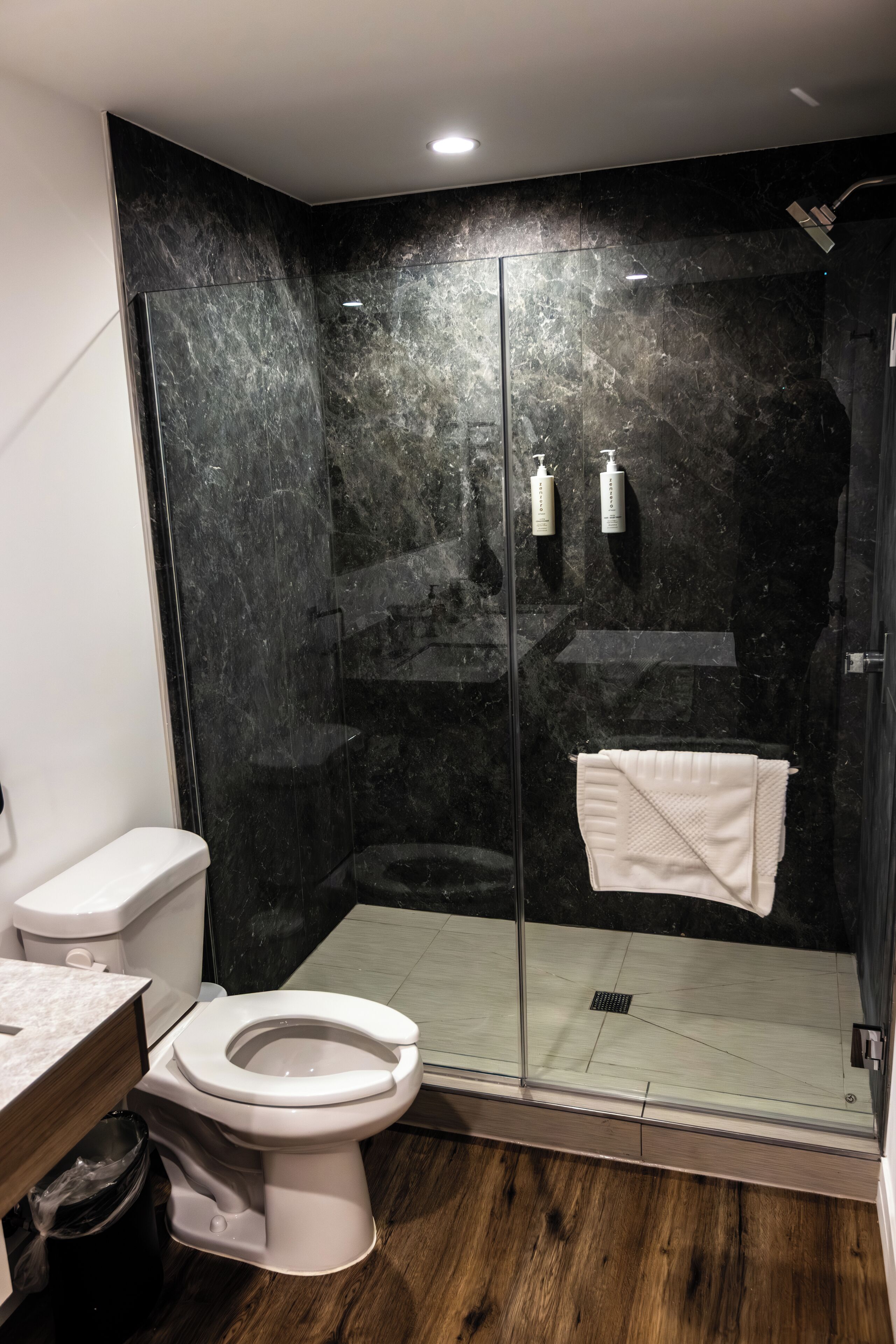 A modern bathroom with a glass-enclosed shower, a white toilet, and a wooden floor.