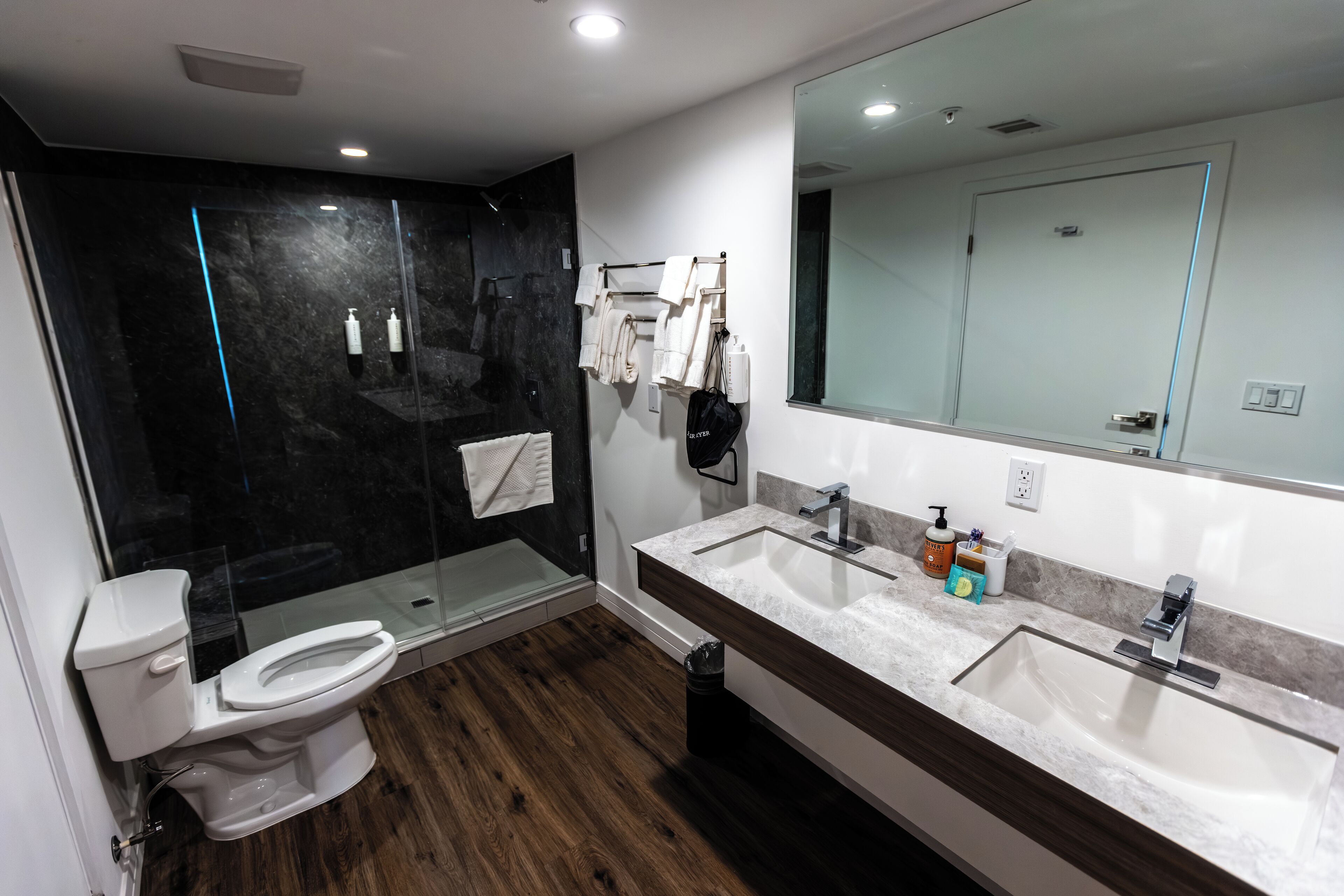 Un baño moderno con ducha de vidrio, inodoro blanco, un espejo grande y tocador doble.
