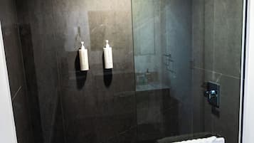 A modern shower area with a glass door, a white towel hanging on the door, and two bottles of shampoo on the wall.