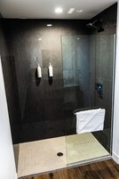 A modern shower area with a glass door, a white towel hanging on the door, and two bottles of shampoo on the wall.